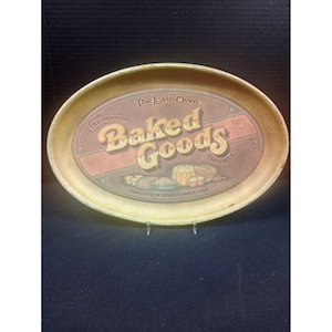Könnte beinhalten: Ein ovales, beigefarbenes Serviertablett mit einer Grafik und dem Text The Lovin'Oven Old Fashioned Baked Goods Company Baking Up A Storm Since 1897. Die zentrale Abbildung zeigt verschiedene Backwaren wie Brot und einen Gugelhupf.