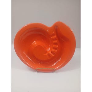 May include: A bright orange ceramic ashtray featuring a distinct spiral design that leads toward the center. The bowl has a smooth, glossy finish with a speckled texture throughout and includes integrated notches along the inner spiral edge.