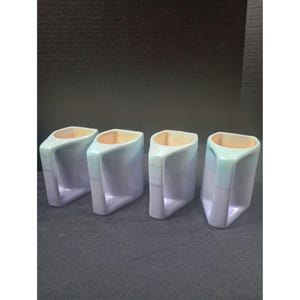 May include: Four ceramic mugs with a unique, angular design. The mugs are a gradient of light blue to white, with a peach-coloured interior. Each mug has a rectangular handle and a geometric shape.