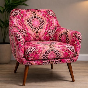 May include: A vibrant armchair featuring a pink and gold leopard print design. The chair has a curved back and armrests, supported by wooden legs. The fabric incorporates pink, gold, and brown hues.