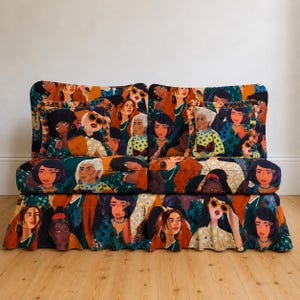 Op de afbeelding: Een tweedelige bank met een levendig patroon met talrijke illustraties van vrouwen gezichten. Het kleurenpalet omvat tinten van teal, oranje en bruin. De bank staat op een houten vloer tegen een witte muur.