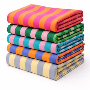 Op de afbeelding: Een stapel van zes opgevouwen strandlakens met kleurrijke streepjespatronen. De handdoeken hebben strepen in verschillende kleuren, waaronder roze, oranje, groen, blauw en geel. De handdoeken zijn netjes opgestapeld en tonen de levendige ontwerpen.