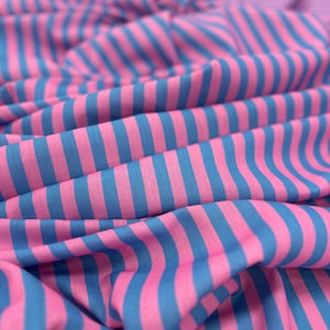 Könnte beinhalten: Nahaufnahme eines Stoffes mit einem sich wiederholenden Muster aus vertikalen Streifen. Die Streifen wechseln sich zwischen leuchtendem Pink und Blau ab. Der Stoff ist drapiert und erzeugt weiche Falten und Schatten.
