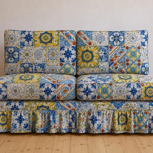 Puede incluir: Un sofá de dos plazas tapizado con tela que presenta un patrón repetitivo de azulejos azules, amarillos y blancos. El sofá incluye dos cojines de respaldo, dos cojines de asiento y una falda base con un diseño de volante fruncido.
