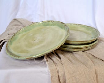 Peut inclure: Un ensemble de quatre assiettes en céramique vertes avec un glaçage brun clair. Les assiettes sont empilées les unes sur les autres et ont un bord légèrement irrégulier.
