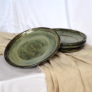May include: Set of four ceramic plates with a green and brown glaze. The plates have a rustic, handmade look and are perfect for serving food.