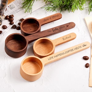 Può includere: Quattro cucchiai da caffè in legno con testo inciso. Due sono marroni scuri, due marroni chiari. Uno recita "Linda & Barry", un altro "The Iuchs Family", un terzo "Richard" e l'ultimo "LIFE HAPPENS, COFFEE HELPS". Sono visibili anche chicchi di caffè e un tappo.