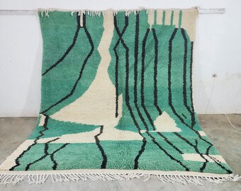 May include: A large, rectangular rug with a teal, cream, and black geometric design. The rug features a soft, textured pile and a fringe along the bottom edge. The design includes vertical black lines and cream-colored shapes.