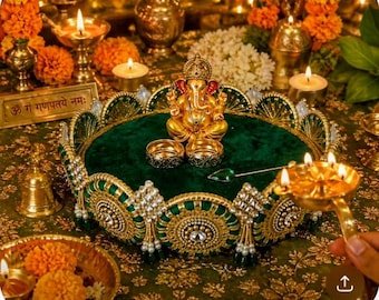 Può includere: Una statua d'oro di Ganesha è posta su un vassoio di velluto verde, circondata da anelli d'oro e un cucchiaio gioiello. Il vassoio è decorato con abbellimenti dorati e verdi. La scena comprende candele accese e composizioni floreali.
