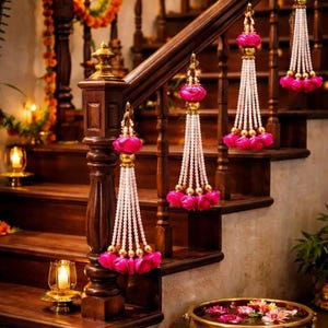 Könnte beinhalten: Eine Holztreppe mit Girlanden und hängenden Ornamenten dekoriert. Die Ornamente bestehen aus weißen Perlen, goldenen Akzenten und rosa Blumenelementen. Am Fuß der Treppe befindet sich eine Messingschale mit schwimmenden Blumen.
