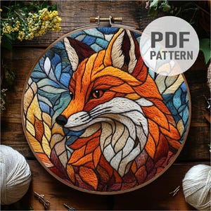 May include: A colorful embroidery pattern of a fox's head with a stained glass effect. The fox is surrounded by leaves and flowers in shades of blue, green, orange, and red.