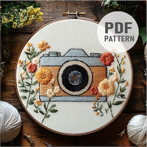 May include: A white embroidery hoop with a vintage camera design surrounded by colorful flowers. The text "PDF PATTERN" is in the upper right corner of the hoop.