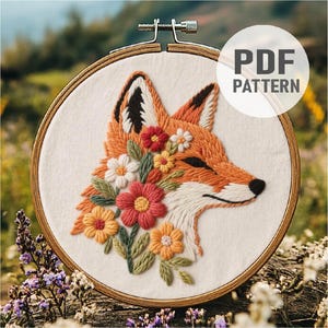 Puede incluir: Cabeza de zorro bordada con detalles florales en un bastidor de madera. El zorro es naranja con puntas de orejas negras y una nariz negra. Las flores son rojas, blancas y amarillas. El texto "PDF PATTERN" está en un círculo blanco.