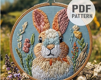 Puede incluir: Arte de bordado en aro con un conejo colorido sobre un fondo azul y detalles florales. El conejo está hecho con una variedad de puntadas y colores, creando un diseño realista y detallado. El aro está hecho de madera y tiene un acabado natural.