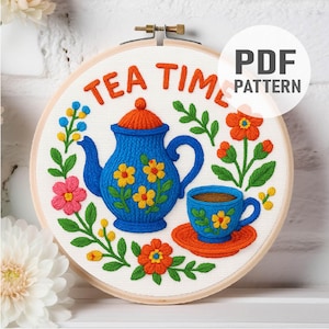 May include: A circular embroidery hoop containing a white fabric panel with a hand-stitched design of a blue teapot and teacup, orange accents, and colorful flowers. The text "TEA TIME" is stitched in orange at the top, with a "PDF PATTERN" label.