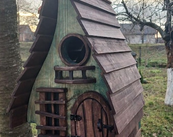 May include: A whimsical wooden birdhouse with a rustic design. The birdhouse features a sloped, shingled roof, a round window, and a small door. The exterior is painted in shades of brown and green, with a small perch below the door.