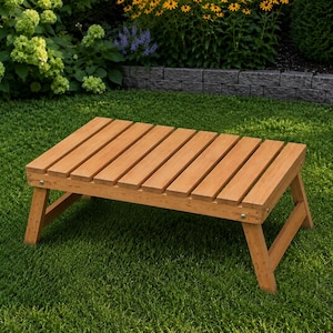 May include: A rectangular wooden outdoor table with a slatted top and angled legs. The table is made of light brown wood and is set on a green lawn. The table is approximately 30 inches long.
