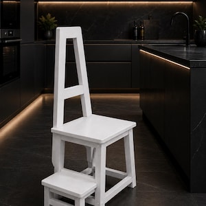 May include: A white wooden step stool chair featuring a tall, rectangular backrest with a central open space and a lower retractable step. The structure is composed of four legs connected by horizontal supports, providing a functional seat.