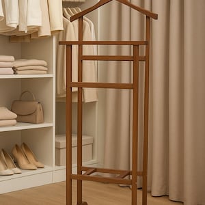 Op de afbeelding: Een houten kledingstandaard met een hanger en meerdere stangen om kleding op te hangen. De standaard heeft een warme bruine kleur en staat in een kast met neutrale kleding en accessoires. De hoogte is ongeveer 150 cm.