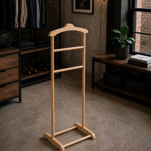 May include: A freestanding valet stand crafted from light-toned wood, featuring a contoured hanger top for garments, two horizontal bars for trousers or accessories, and a sturdy rectangular base with two parallel feet for stability.