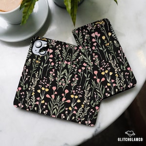 May include: Two black phone cases featuring a floral design. The pattern includes pink and yellow flowers on black stems. The cases are made from a robust material and are designed to safeguard your phone from scratches and drops.