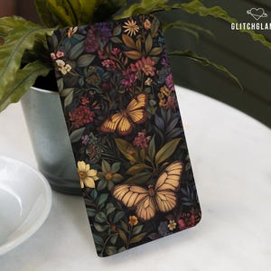Könnte beinhalten: Eine schwarze Handyhülle mit einem Blumenmuster und zwei gelben Schmetterlingen. Die Blumen sind in den Farben Rosa, Lila und Blau gehalten.