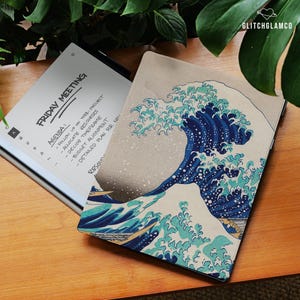 May include: A digital tablet with a screen displaying a "Friday Meeting" agenda. A cover with a Japanese wave design is next to the tablet. The cover features shades of blue and white, with the text "GLITCHGLAMCO" in the upper right corner.