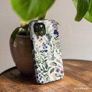 May include: A white phone case with a floral pattern featuring blue, purple, and green flowers. The case has a cutout for the camera lens.