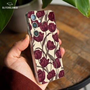 Op de afbeelding: Transparante telefoonhoes met een bloemenpatroon van bordeauxrode tulpen op een crèmekleurige achtergrond. De hoes heeft een glanzende afwerking en is ontworpen voor een smartphone. De merknaam "GLITCHGLAMCO" is linksboven zichtbaar.