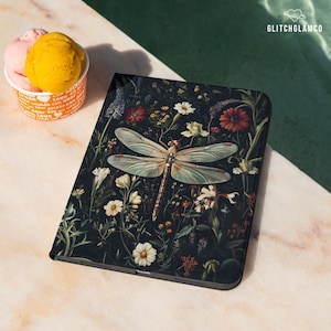 May include: A black tablet case with a floral and dragonfly design. The case has a dark background with colorful flowers and a large dragonfly in the center. The GlitchGlamco logo is in the top right corner.