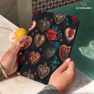 May include: A black tablet case featuring a repeating pattern of ornate, gold-framed hearts, red roses, and blue leaves. The case is held by a person. The text "GLITCHGLAMCO" is visible in the upper right corner.