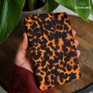 Op de afbeelding: Een rechthoekige telefoonhoes met een schildpadpatroon in zwart en oranje tinten. De hoes heeft afgeronde hoeken en een gladde afwerking. Het GlitchGlamCo-logo is rechtsboven zichtbaar.