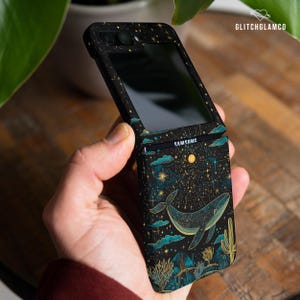 Puede incluir: Funda de teléfono negra con un diseño de ballena celestial. La funda presenta una ballena, nubes, estrellas y cactus en verde azulado y dorado sobre un fondo negro. La funda es para un teléfono Samsung.