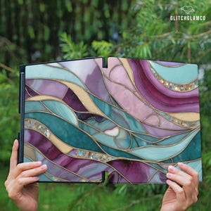 May include: A decorative panel with a stained glass design. The panel features a flowing pattern of teal, purple, pink, and gold colors. The text "GLITCHGLAMCO" is in the upper right corner. The panel is held by hands against a blurred green background.