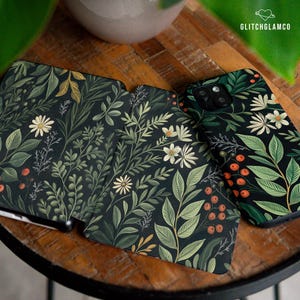 Könnte beinhalten: Drei Handyhüllen mit dunkelgrünem Hintergrund und einem floralen Muster. Das Design umfasst weiße Blumen, grüne Blätter und rote Beeren. Die Hüllen sind aus strapazierfähigem Material gefertigt und schützen Ihr Handy vor Kratzern und Stürzen.