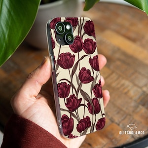 May include: A clear phone case featuring a burgundy tulip floral pattern on a cream background. The case has a glossy finish and is designed to fit a smartphone. The phone case is held in a person's hand.