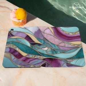 Pu&ograve; includere: Custodia per tablet con un design a vetrata colorata nei toni del verde acqua, viola e oro. La custodia presenta un motivo astratto e fluido con dettagli dorati. Il logo GlitchGlamCo &egrave; visibile.