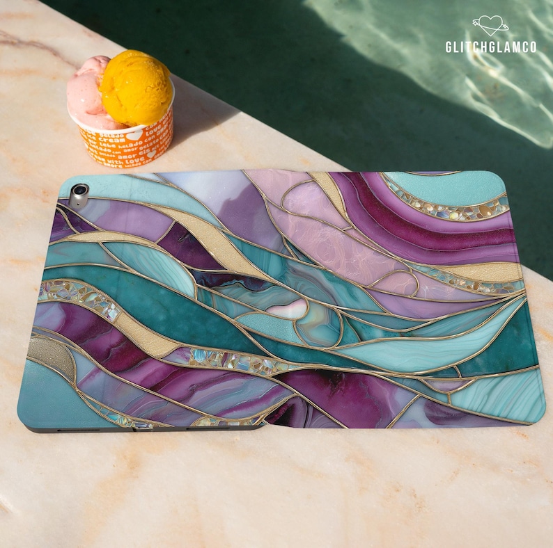 Pu&ograve; includere: Custodia per tablet con un design a vetrata colorata nei toni del verde acqua, viola e oro. La custodia presenta un motivo astratto e fluido con dettagli dorati. Il logo GlitchGlamCo &egrave; visibile.