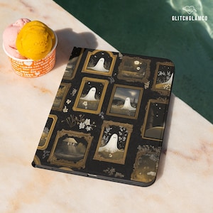 Pode incluir: Capa de tablet preta com um padrão repetido de ilustrações de fantasmas emolduradas em ouro. O design inclui flores brancas e um fundo escuro. A capa é mostrada ao lado de uma taça de sorvete.