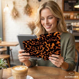 Op de afbeelding: Een persoon houdt een tablet vast met een hoesje met schildpadpatroon. De hoes heeft een herhalend patroon van donkerbruine en oranje vlekken. De tablet zit in een doorzichtige beschermhoes. De persoon glimlacht en kijkt naar de tablet.