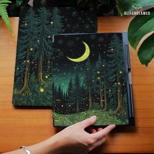 May include: Two black tablet covers with a forest scene. The covers feature tall green trees, glowing yellow fireflies, and a crescent moon against a dark night sky. The design has a whimsical, fantasy theme.