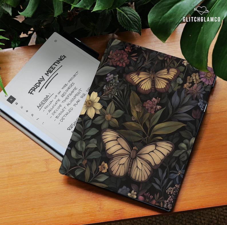 May include: A digital tablet with a floral butterfly design cover rests on a wooden surface next to an open tablet displaying a meeting agenda. The cover features butterflies and flowers in shades of beige, brown, and purple against a dark background.