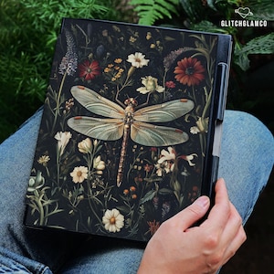 May include: A black tablet case featuring a detailed illustration of a dragonfly with intricate wing patterns, surrounded by a variety of flowers in shades of red, white, and yellow. The text "GLITCHGLAMCO" is visible in the upper right corner.