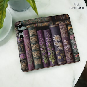 May include: A rectangular smartphone case featuring a printed design of vintage book spines with floral illustrations in shades of purple, green, and gold. The case includes a camera cutout on the top left corner and the text GLITCHGLAMCO at the top right.