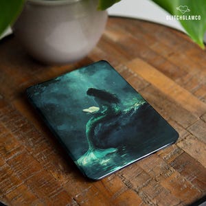 Könnte beinhalten: Ein dunkelblauer und grüner digitaler Buchumschlag mit einer Meerjungfrau, die auf einem Felsen im Meer ein Buch liest.