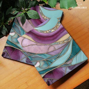 May include: Two decorative coasters with a stained glass design. The coasters feature a mix of purple, teal, and gold colors with a swirling pattern. The coasters are on a wooden surface. The text "GLITCHGLAMCO" is visible in the upper right corner.