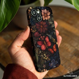 May include: A black phone case featuring a floral and butterfly design. The case has a dark background with red, orange, and yellow flowers and butterflies. The case is held in a hand.