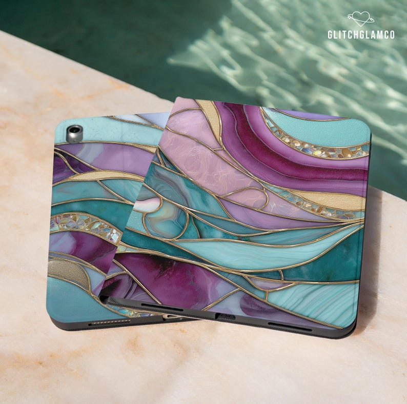 Pu&ograve; includere: Due custodie per tablet con un design a vetrata. Le custodie presentano un mix di colori turchese, viola, rosa e oro. Le custodie sono su una superficie chiara con una piscina sullo sfondo. Il testo "GLITCHGLAMCO" si trova nell'angolo in alto a destra.