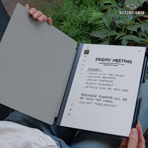 May include: A gray digital notepad with a black pen. The screen displays handwritten notes for a Friday meeting, including agenda items and resource planning notes. The notepad is open, revealing the screen and the cover.