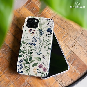 May include: A white phone case with a floral pattern featuring green leaves, blue and purple flowers, and black berries. The case has a clear back and a raised camera bump.
